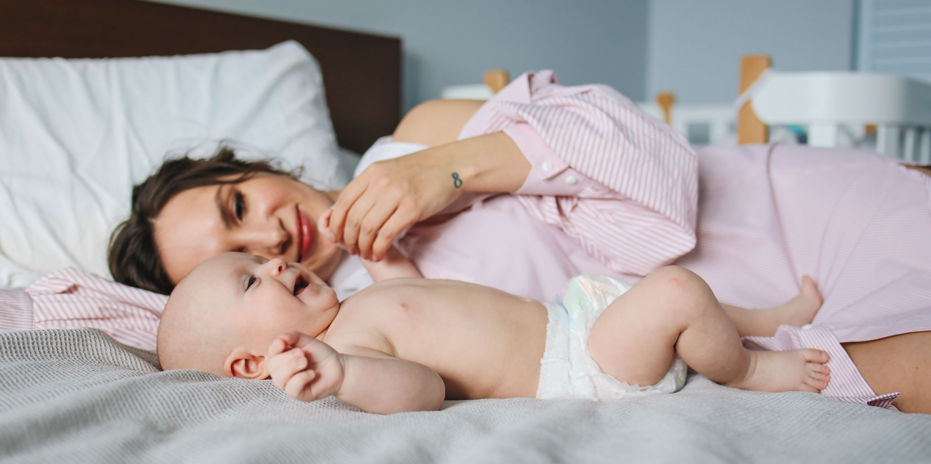 A mother and her baby enjoy a tender moment together, lying on a cozy bed.