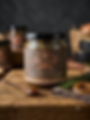 Jar of Honey & Rosemary Balsamic Onion jam on wooden table with spoon filled with onion jam and fresh rosemary beside