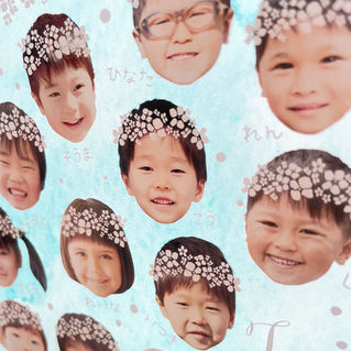 ブルースカイの背景に花冠をつけた子どもたちの顔写真が並ぶ、卒園記念アクリルスタンドの拡大画像(名前入り)