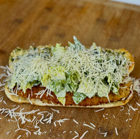 Shredded lettuce and cheese atop a crispy chicken cutlet sandwich on a wooden cutting board