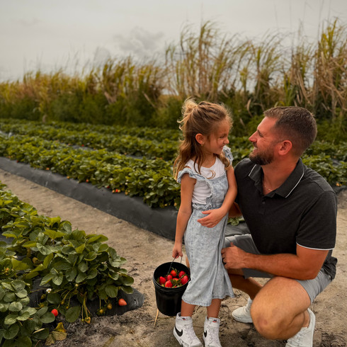 A young girl and her in dad standing in a strawberry field holding buckets of freshly picked strawberries