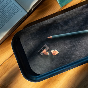 Trousse noire, crayon gris, taille-crayon et copeaux sur une table en bois.