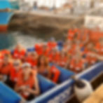 People in orange life vests smile on a blue boat labeled "EXPRESS" docked at a marina. Sunlight casts a warm glow. to little corn island