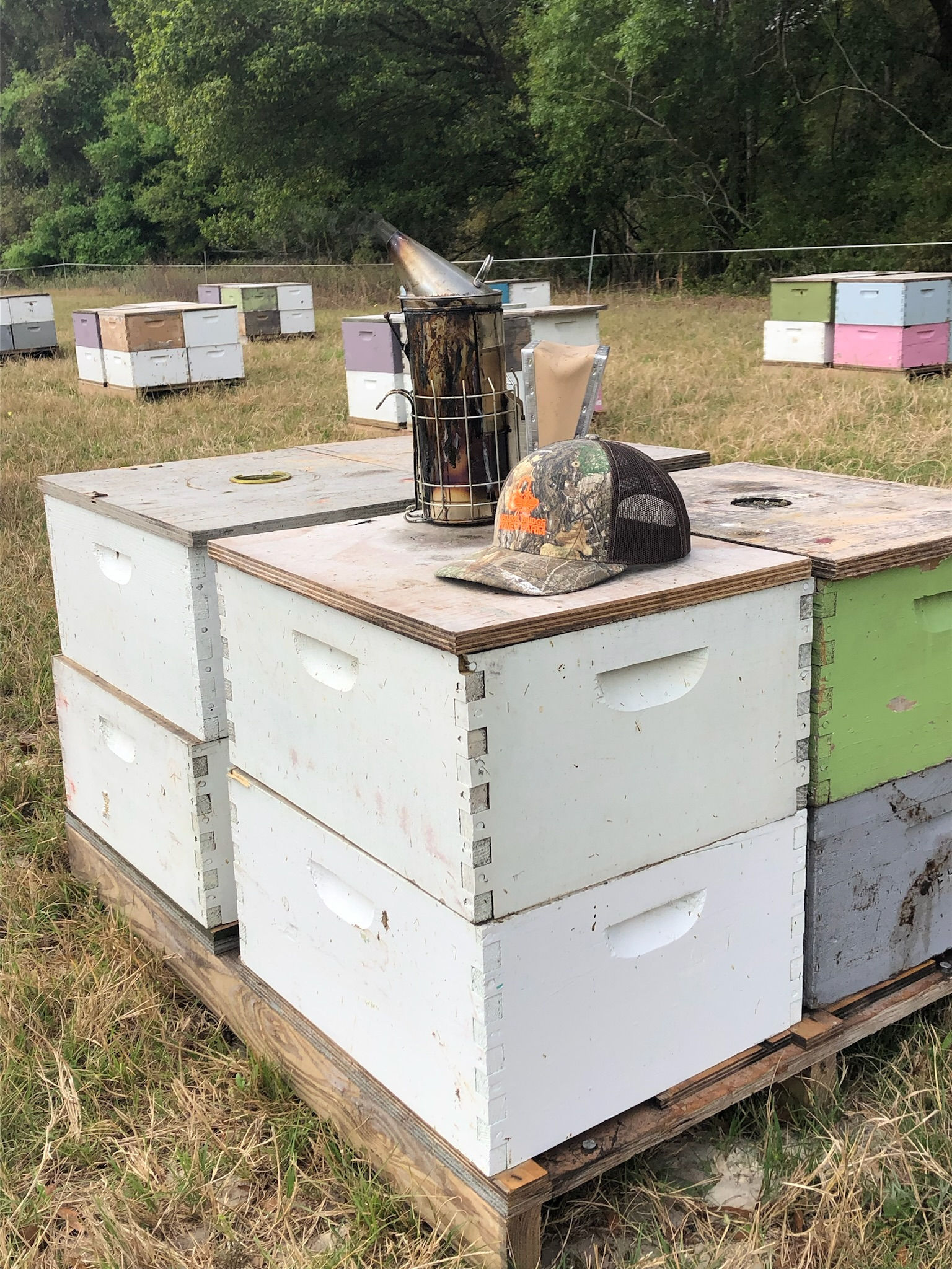 a bee smoker and an embroidered richardson brand hat sitting on top of a pallet of bee boxes
