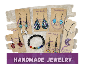 Handmade jewelry from Cat-Tastic Wonders displayed on a neutral cream background, including earrings, necklaces and other handcrafted accessories.