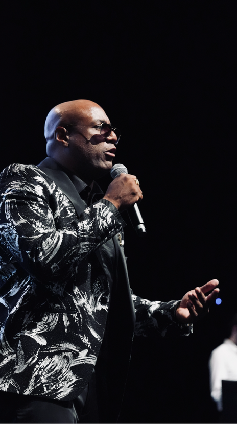 a bald man singing into a microphone in a black and white suit