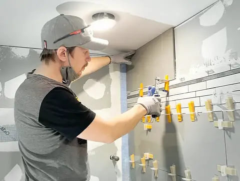 Kanata technician finishing bathroom renovation by meticulously adjusting tile spacers for even grout lines.