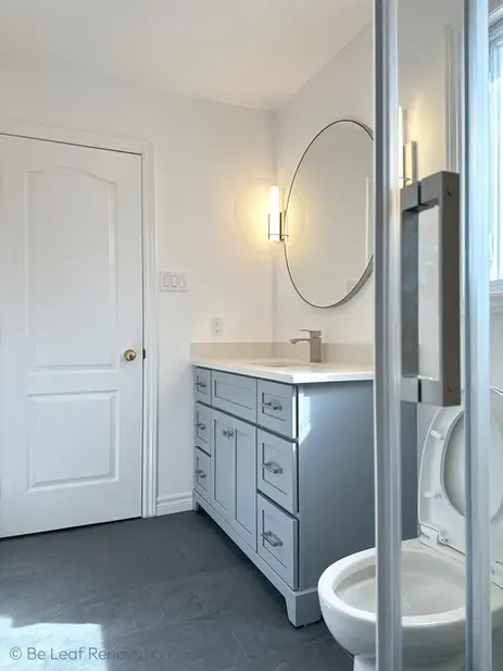 Close-up of gray bathroom vanity, chrome faucet, round mirror, wall sconce