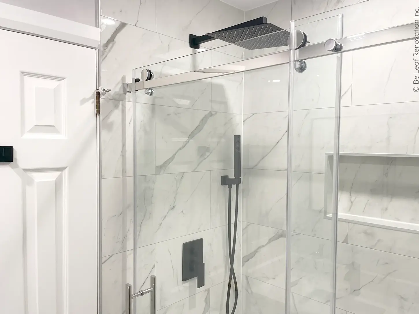 Walk-in glass shower, matte black fixtures, marble tiles