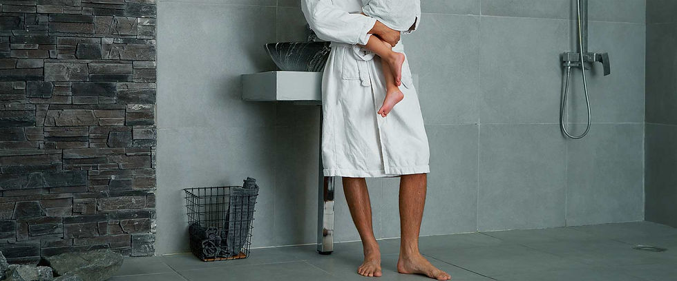 Father in a bathrobe holding his daughter in pajamas near a shower enclosure and basket