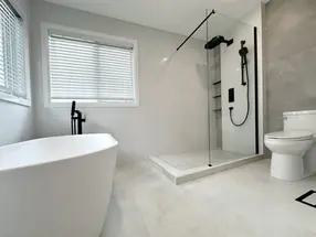 Freestanding tub, curbed glass shower enclosure with black fixtures, and simple toilet.