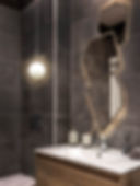 Elegant bathroom interior with dark tiles, unique geometric mirrors, round pendant light, wooden vanity, soap dispensers, and reed diffuser on sink.