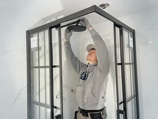 Installer attaches black rainfall shower head in glass shower enclosure.