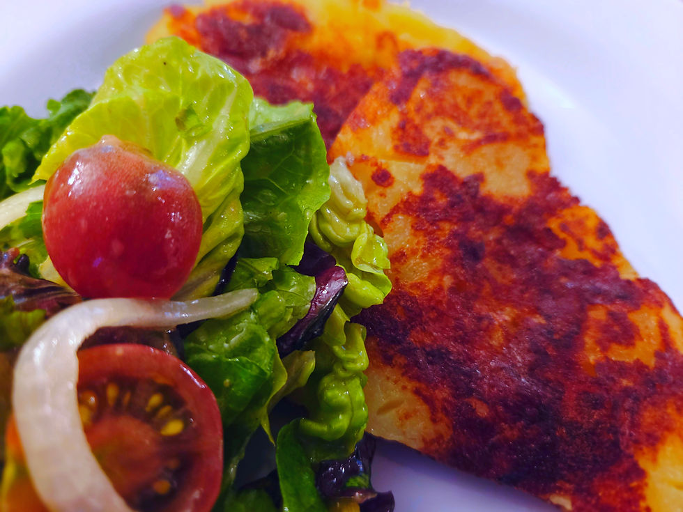 A white plate of frico topped with a salad of lettuce, tomatoes, and onions.