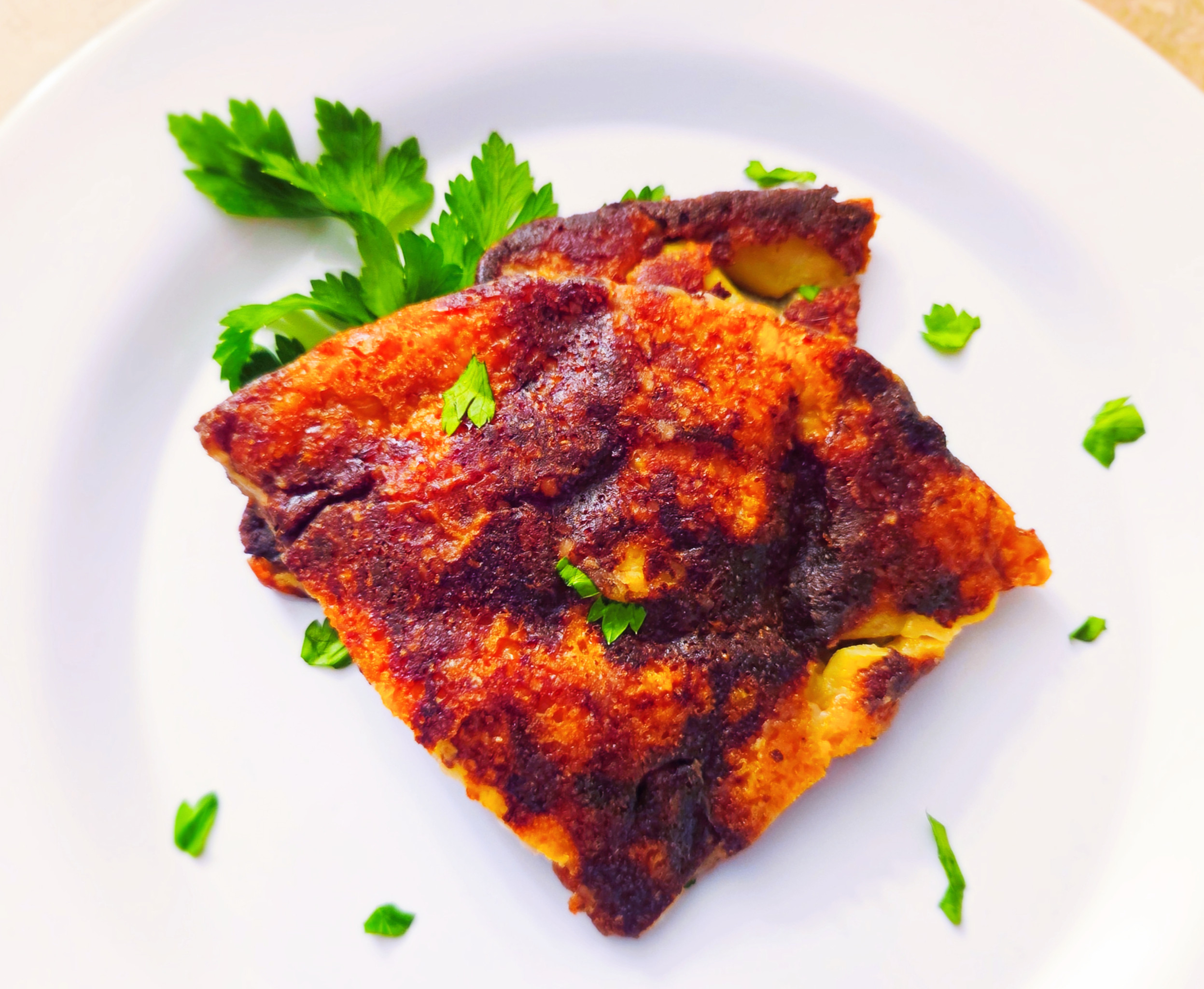 Potato and onion frico on a white plate garnished with fresh parsley.