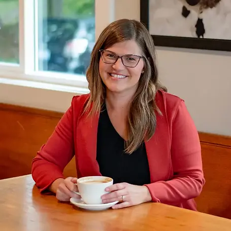 Meg Laidlaw, founder of Profound Wellness and Board Certified Nurse Coach, smiling while enjoying a latte at a cozy café table.