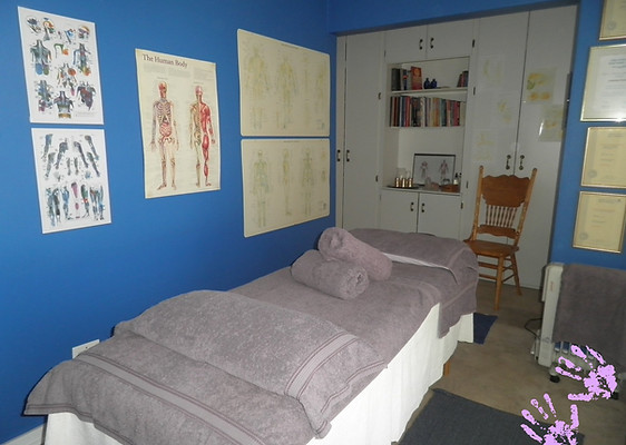Massage room with a massage bed made up with towels. There are anatomical posters on the wall.