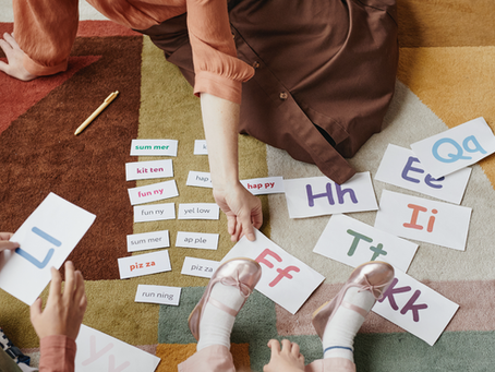 A mom and children play with colorful letter cards during a learning activity. They are all sitting on a colorful carpet.
