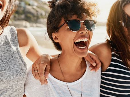 Three women laugh while walking on the beach during the summer.