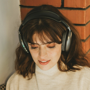 A woman in a white sweater listens to music or a podcast with black headphones upon her head.