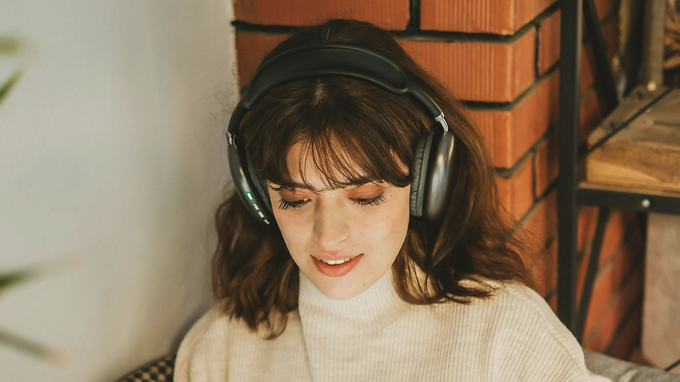 A woman in a white sweater listens to music or a podcast with black headphones upon her head.