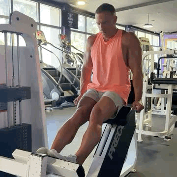 Theo Marcopoulos homme en débardeur orange faisant un exercice sur machine de musculation dans une salle de sport, concentré.