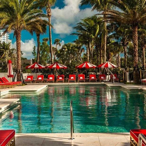Enjoy your Miami Beach stay and fitness journey with Theo Marcopoulos at the luxurious Faena pool, surrounded by vibrant red and white sun loungers and palm trees.
