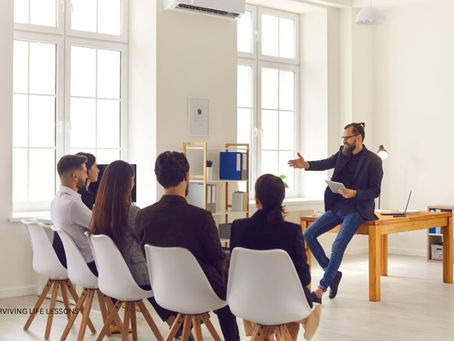 A male supervisor or leader speaking to a small team of five employees, demonstrating mentorship, knowledge sharing, and team collaboration.