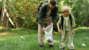 A father and son collecting trash in a park while the sun shines, symbolizing care for the environment and personal responsibility.