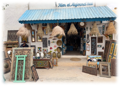 Djerbahood: Boutique artisanale avec objets décoratifs colorés et paniers exposés. Enseigne "Hier et Aujourd'hui" sur fond blanc et bleu. Atmosphère chaleureuse.