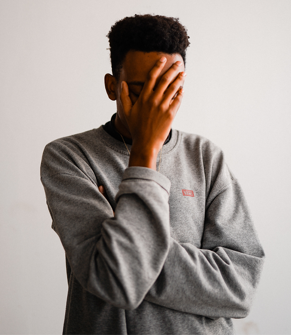 Person in a gray sweater covering face with hand, standing against a plain background.