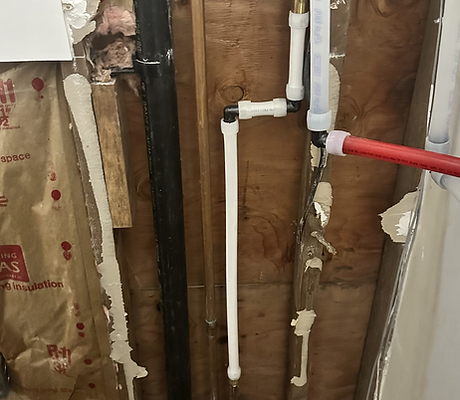 New white PVC and red PEX water supply pipes rough-in inside an open wall cavity with exposed wood studs