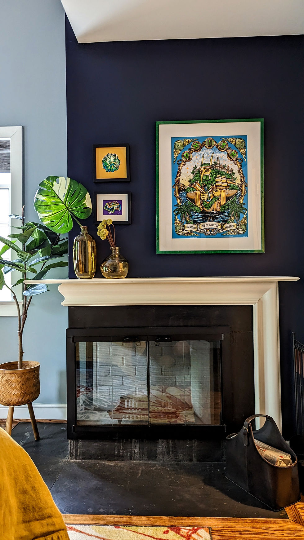 A variegated monstera leaf in glass jars, on a navy fireplace mantel, and Phish artwork