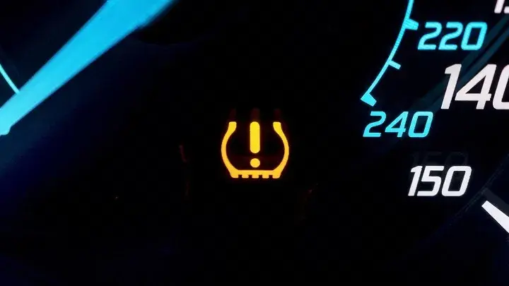 Yellow tire pressure monitoring system (TPMS) warning light on a dashboard, indicating low tire pressure in one or more tires.