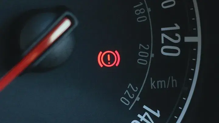 Red brake warning light with an exclamation mark on a car dashboard, indicating a potential issue with the braking system or parking brake.