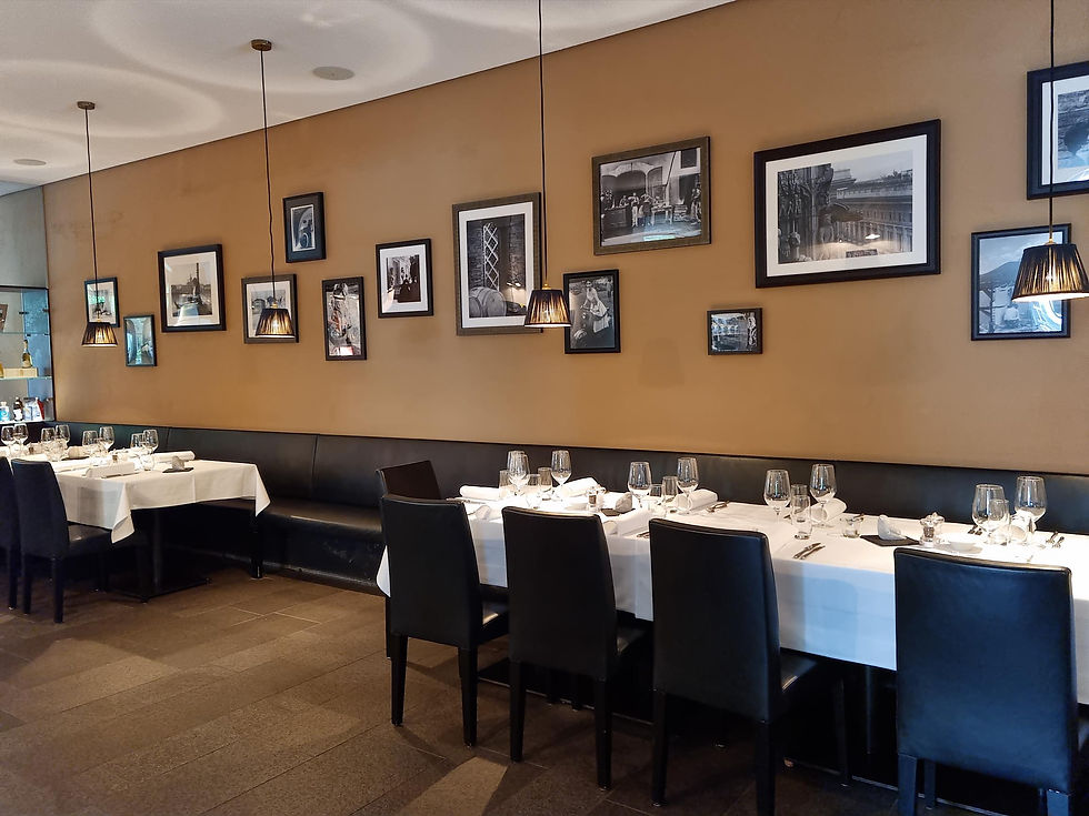 Elegantes Restaurant mit gedeckten Tischen, schwarzen Stühlen und brauner Wand mit gerahmten Bildern. Gemütliche, einladende Atmosphäre.