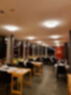 Elegantes Restaurant mit gedeckten Tischen, Kerzen und Glaswänden. Warmes Licht, ruhige Atmosphäre, Blick auf beleuchtete Stadt.