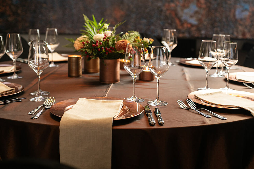 Eleganter gedeckter Tisch mit bronzefarbenen Tellern, Kerzen, Gläsern und Blumenarrangement, vermittelt eine festliche Atmosphäre.