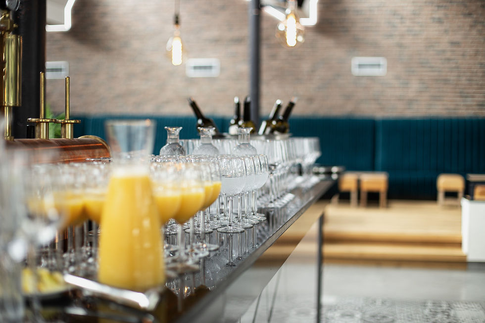 Gläser und Flaschen auf einer Theke, dahinter eine Backsteinwand. Modernes Café-Ambiente mit gemütlichen Sitzgelegenheiten im Hintergrund.