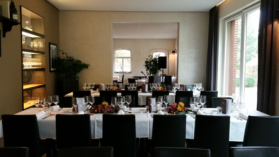 Elegantes Restaurant mit gedeckten Tischen, weißen Tischdecken, Blumenarrangements und Gläsern. Heller Raum mit großen Fenstern.