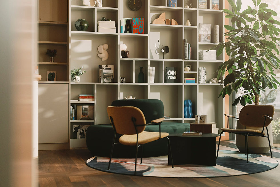 Gemütliche Leseecke mit Sessel, Tisch und Regalwand voller Bücher und Dekorationen. Großes Fenster und Pflanzen schaffen eine ruhige Atmosphäre.