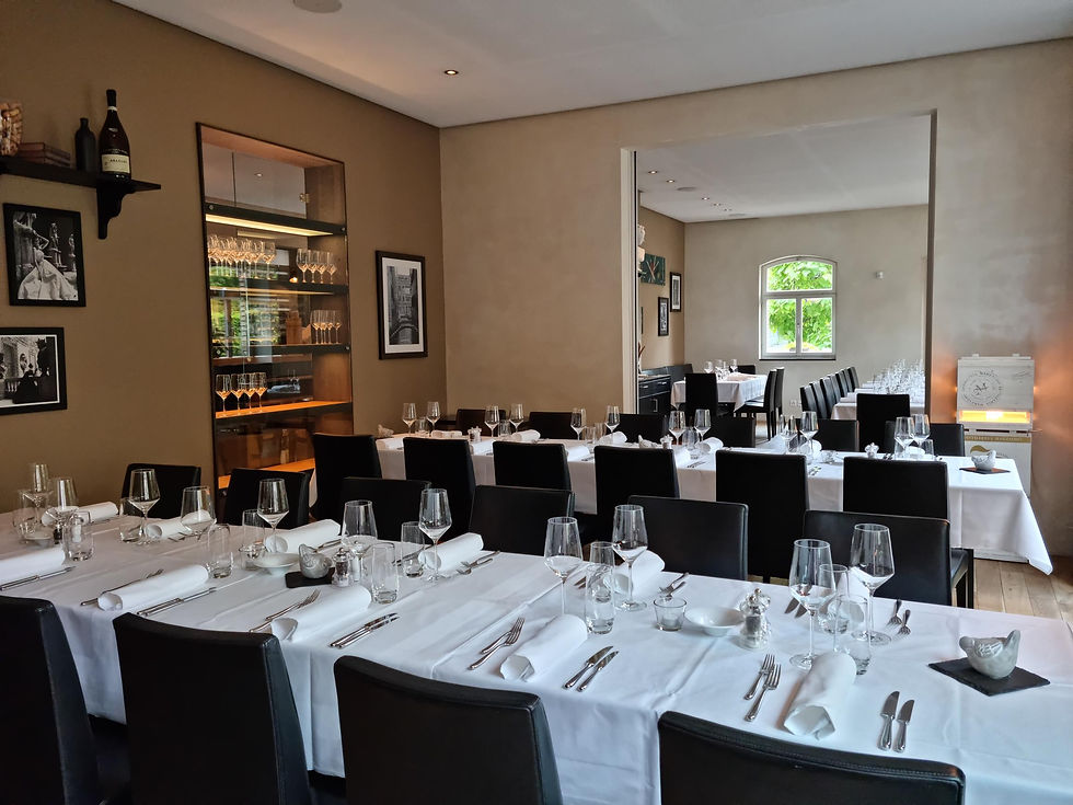 Elegantes Restaurant mit gedeckten Tischen, weißen Tischdecken, Gläsern und Besteck. Braune Wände, Fotos, Fenster mit grünem Blick.