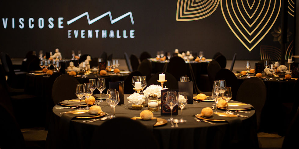 Elegant gedeckter Veranstaltungstisch mit Kerzen und Brot, schwarzes Tischtuch, im Hintergrund leuchtet "Viscose Eventhalle" an der Wand.