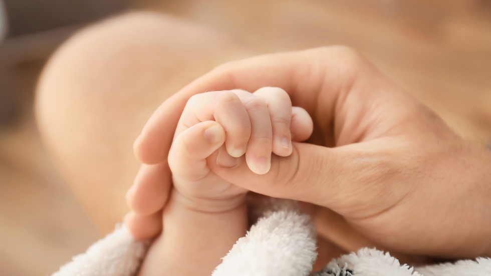 Baby's hand gently grasps an adult's thumb, conveying warmth and connection.