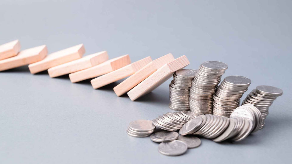 Stacks of silver coins on a gray surface with light wooden dominoes falling towards them.