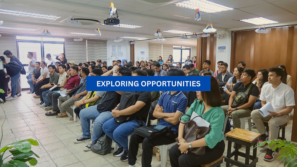 Audience in a room attentively listening, with a "Exploring Opportunities" banner. Bright lighting, indoor plants, and decorative ceiling.
