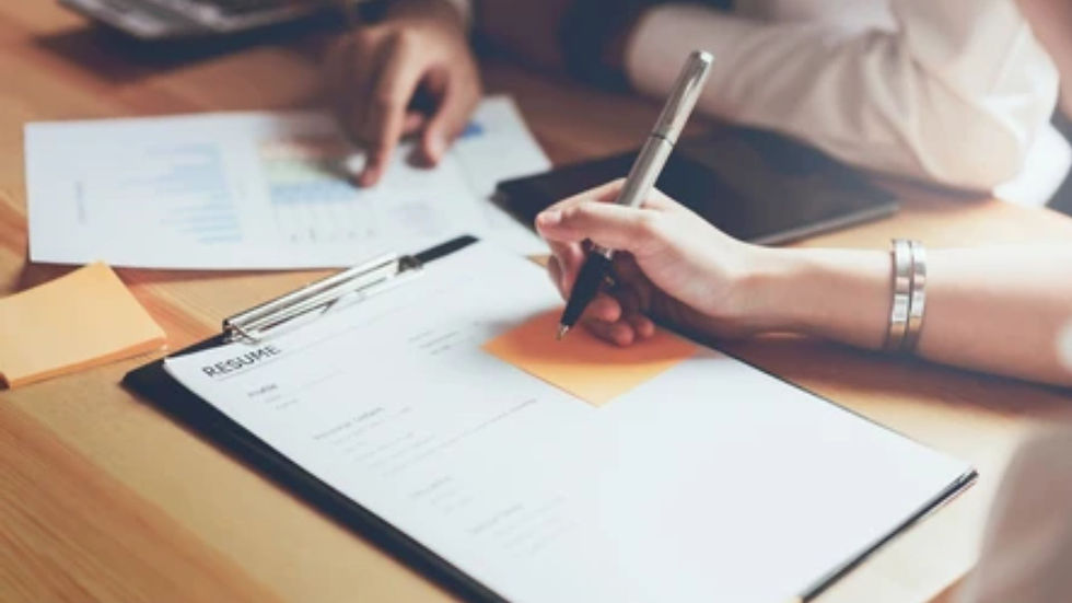 Hands on a wooden table, one writing on a resume with a pen, surrounded by graphs and sticky notes. Professional setting.