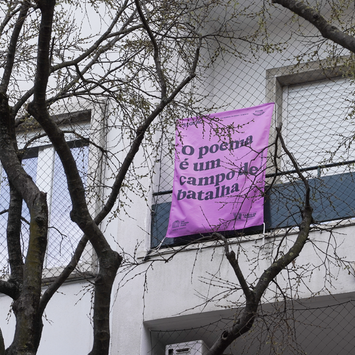 Bandeira em varanda com o verso “O poema é um campo de batalha”, de Gisela Casemiro.