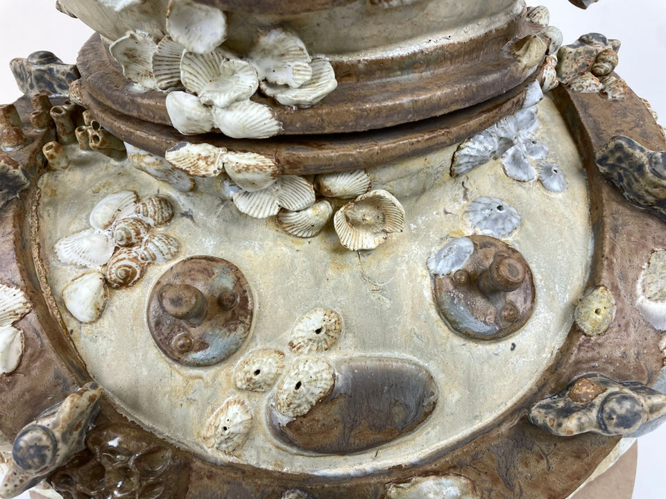 A close-up of a clay diver's helmet collar, covered with coral and shells, in shades of beige and yellow.