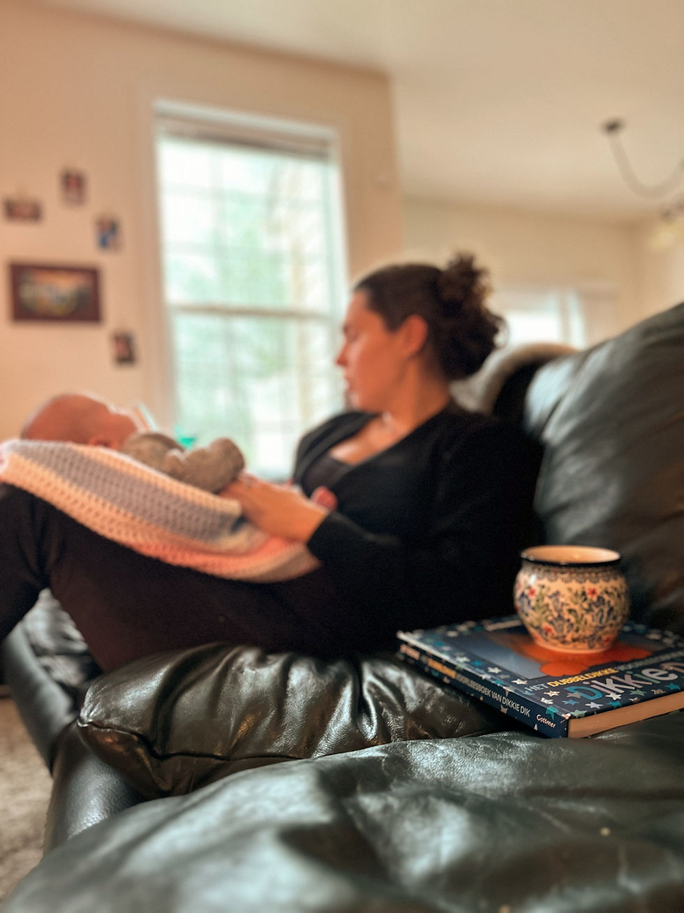 Mom sitting on the couch with her newborn on her lap, relaxing and bonding, next to her a warm cup of tea